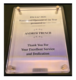 Close-up of a clear acrylic award plaque mounted with metal standoffs. The plaque reads, “RWAAZ 2026 Wastewater Operator of the Year presented to Andrew French. Thank You For Your Excellent Service and Dedication.”