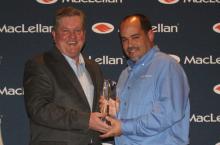 John Evans (left) presenting the engraved cyrstal leadership award to Robby Clendening (right) in front the the photo backdrop with the MacLellan logo repeated across it. 